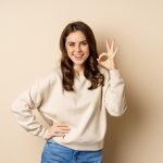 excellent smiling beautiful woman showing okay ok zero sign approve smth good praising complimenting beige background